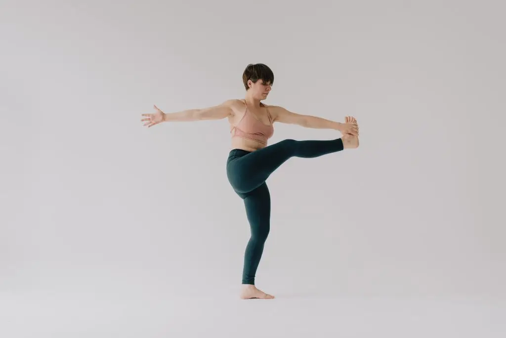 Magdalena in Leggings dehnt ihr Bein in einer stehenden Yoga Drehhaltung